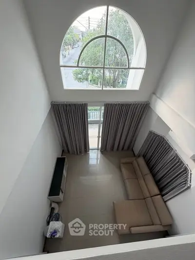 Spacious living room with high ceiling and large arched window offering a serene view.