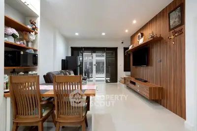 Modern living room with wooden accents and open dining area, featuring sleek furniture and bright lighting.