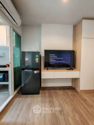 Modern living room with sleek TV setup and compact fridge, featuring stylish wood flooring and contemporary design.