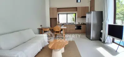 Modern open-layout living room with kitchen, featuring sleek furniture and natural light.