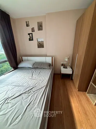Cozy bedroom with wooden flooring and large window offering natural light.