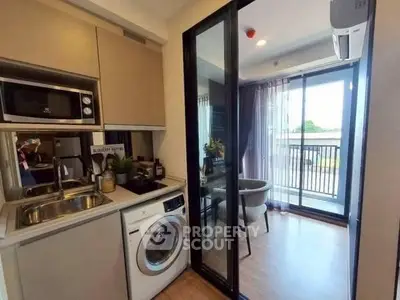 Modern kitchen with washing machine and open layout leading to a bright balcony view.