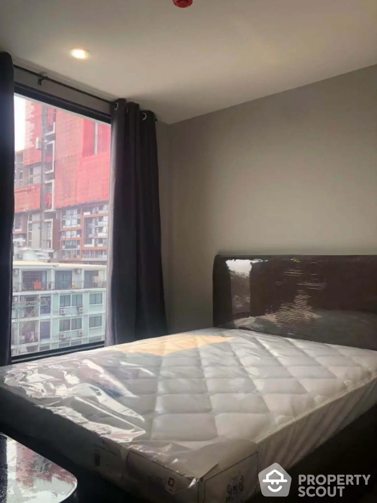 Modern bedroom with large window and city view, featuring a new mattress and sleek design.