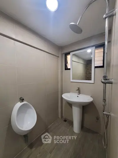 Modern bathroom with sleek fixtures and neutral tiles, featuring a shower and urinal.
