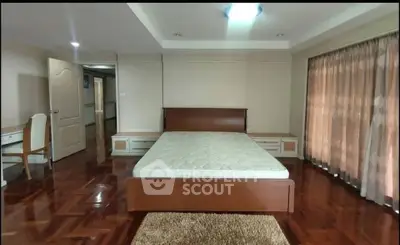 Spacious bedroom with wooden flooring and large windows for natural light.