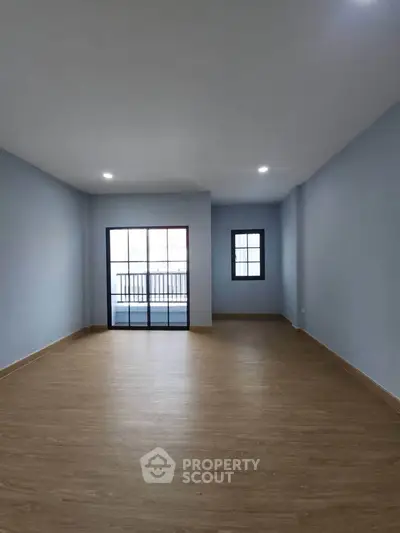 Spacious empty room with wooden flooring and large windows for natural light.