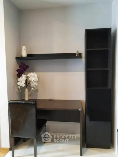 Modern study nook with sleek black desk, chair, and shelving, accented by elegant decor and flowers.