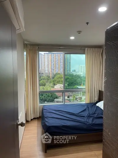 Cozy bedroom with large window offering stunning cityscape views, perfect for urban living.