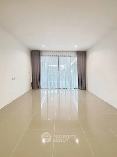Spacious empty room with glossy tiled floor and large window with curtains.