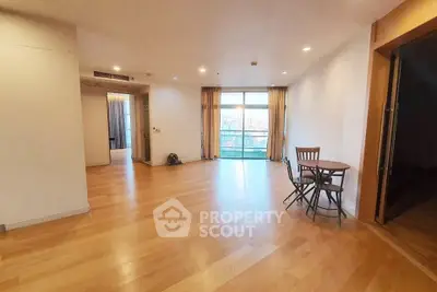 Spacious living room with wooden flooring and large windows offering natural light and city views.
