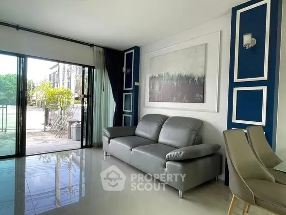 Modern living room with sleek grey sofa and large glass doors opening to a patio.