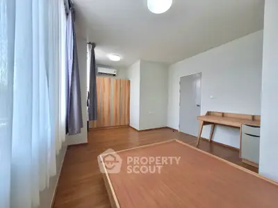 Spacious and well-lit bedroom with polished wooden floors, large windows with curtains, and built-in wardrobe, ideal for comfortable living.