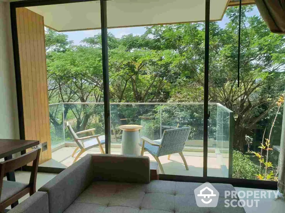 Serene living room with large glass doors opening to a lush balcony view, modern furniture, and abundant natural light.