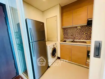 Modern compact kitchen with stainless steel fridge and washing machine in cozy apartment.