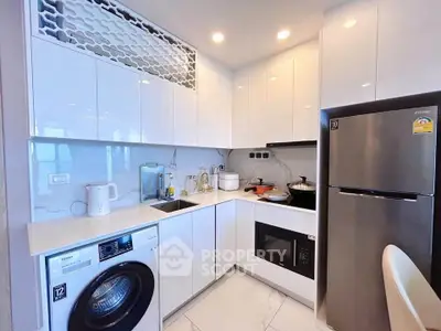 Modern kitchen with sleek white cabinets, stainless steel fridge, and built-in washing machine.