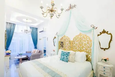 Luxurious bedroom with elegant decor and chandelier, featuring a cozy seating area and ornate bed frame.