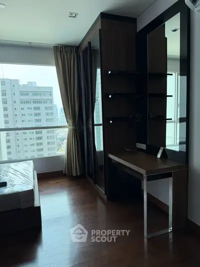 Modern bedroom with large window and city view, featuring sleek wooden furniture and ample natural light.