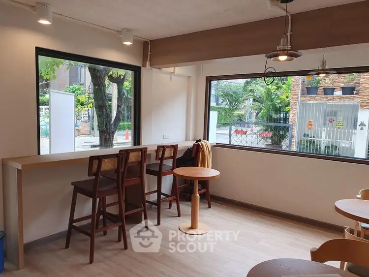 Charming cafe-style seating area with large windows and wooden furniture, perfect for relaxation.