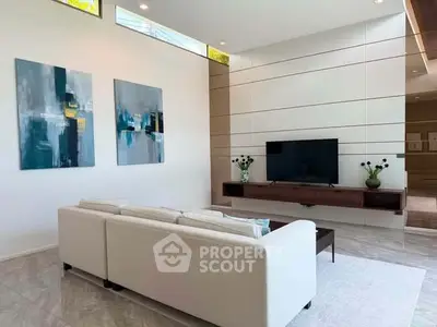Modern living room with sleek design, featuring a white sofa, wall-mounted TV, and abstract art pieces.