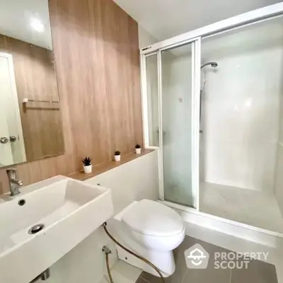 Modern bathroom with sleek fixtures, including a full bathtub with glass enclosure, a stylish basin, and a well-placed toilet, accented by warm wooden tones.