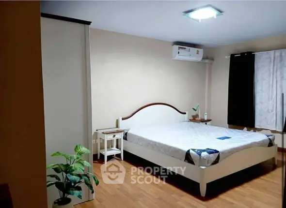 Spacious bedroom with wooden flooring and modern air conditioning unit.