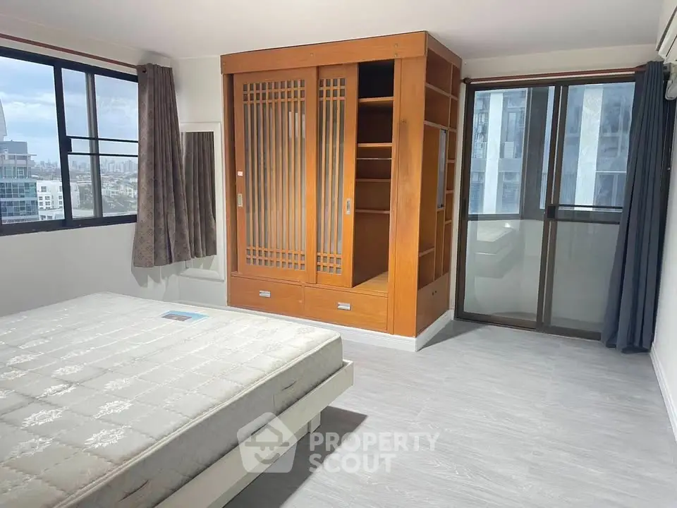 Spacious bedroom with large windows and built-in wooden wardrobe in modern apartment.