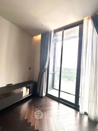 Elegant room with large window and city view, featuring dark wood flooring and modern curtains.