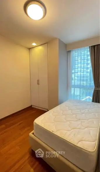 Cozy bedroom with wooden flooring and large window offering city view