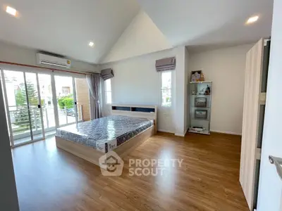 Spacious bedroom with wooden flooring and balcony access in modern home.