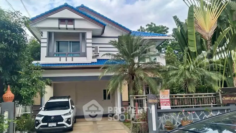 Charming two-story house with blue roof, lush garden, and spacious driveway in a serene neighborhood.