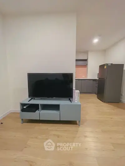 Modern living room with sleek TV stand and open kitchen layout, featuring wooden flooring and contemporary design.
