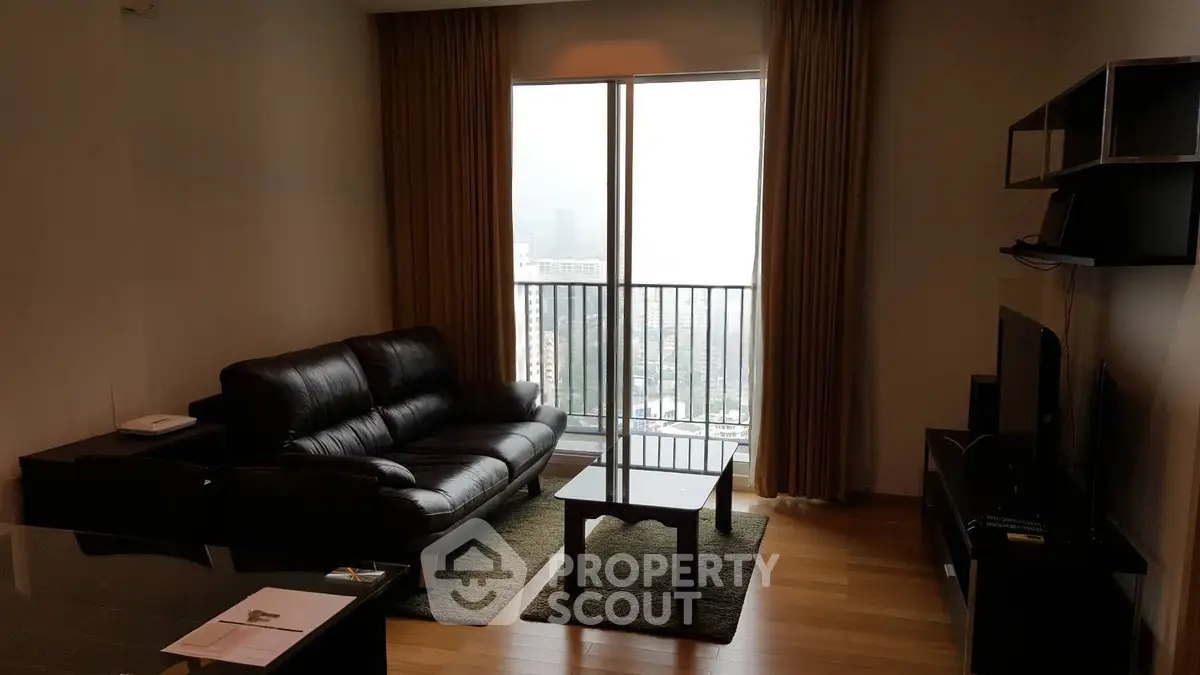 Modern living room with leather sofa and city view balcony in high-rise apartment.