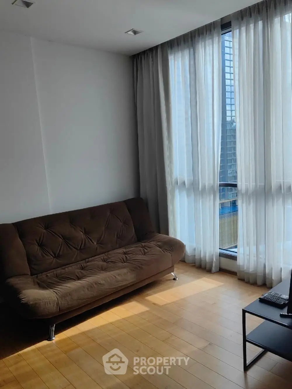 Modern living room with large windows and brown sofa, offering abundant natural light and city views.