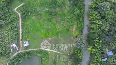 Aerial view of lush green land with river and pathways, ideal for development.
