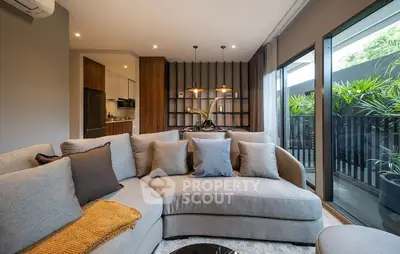 Luxurious modern living room with plush sectional sofa and floor-to-ceiling windows overlooking lush greenery.