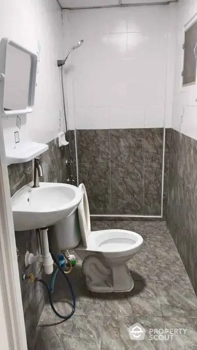 Compact bathroom with tiled walls and floor, featuring a shower and toilet.