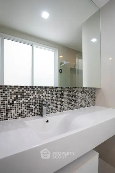 Modern bathroom with sleek sink and mosaic tile backsplash, featuring a large mirror and natural light.