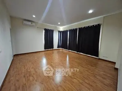 Spacious empty room with wooden flooring and large windows, ideal for customization.