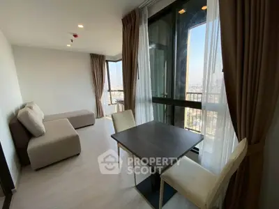Modern living room with large windows and city view, featuring a cozy sofa and dining table.