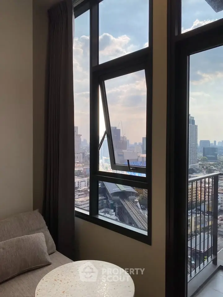 Stunning city view from modern high-rise apartment with large windows and cozy seating area.