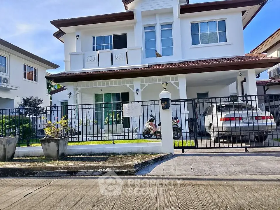 Charming two-story white house with balcony and gated driveway in a serene neighborhood.