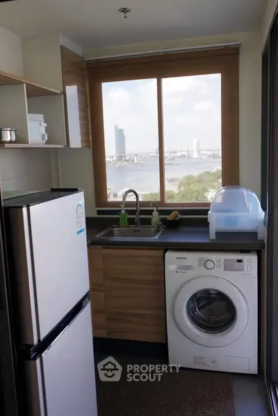 Modern kitchen with river view, featuring washing machine and compact fridge.