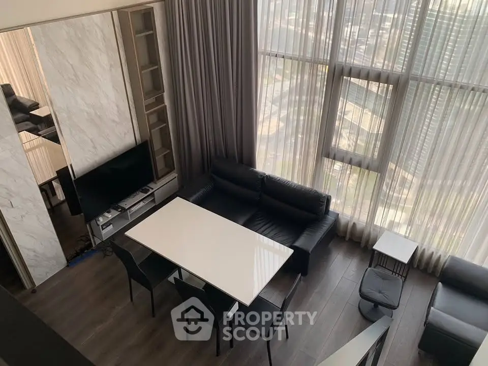 Modern living room with high ceilings and large windows offering city views.