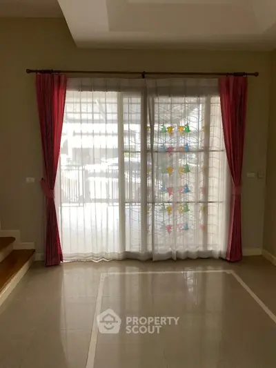 Spacious and well-lit living space with gleaming tiled floors and elegant red drapery framing a large window, inviting ample natural light.