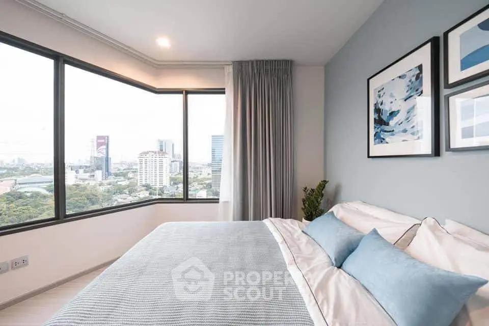 Modern bedroom with large windows offering stunning city views, featuring elegant decor and cozy bedding.