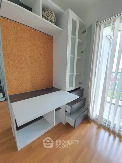 Modern study area with built-in desk and storage, featuring corkboard and glass cabinet doors.