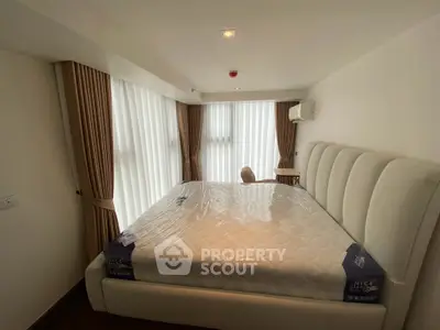 Spacious bedroom with large windows and elegant curtains in modern apartment.