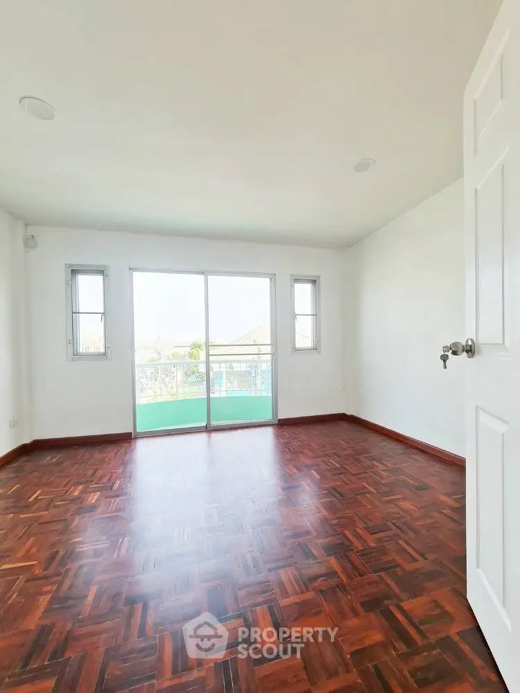 Spacious empty room with wooden flooring and balcony access, perfect for customization.