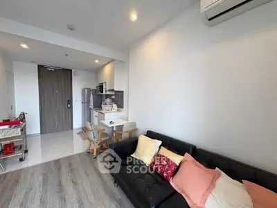 Modern living room with open kitchen, featuring sleek furniture and air conditioning.