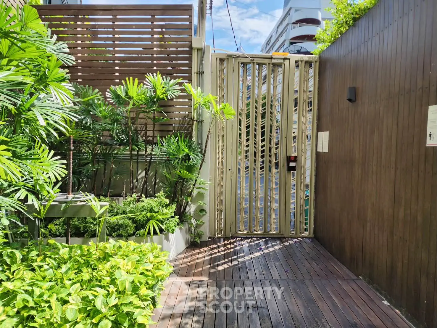 Modern gated entrance with lush greenery and wooden accents, offering a serene and secure ambiance.